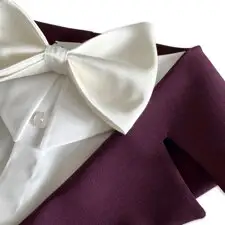 Primer plano de la pajarita de raso marfil sobre la camisa blanca del arnés esmoquin burdeos